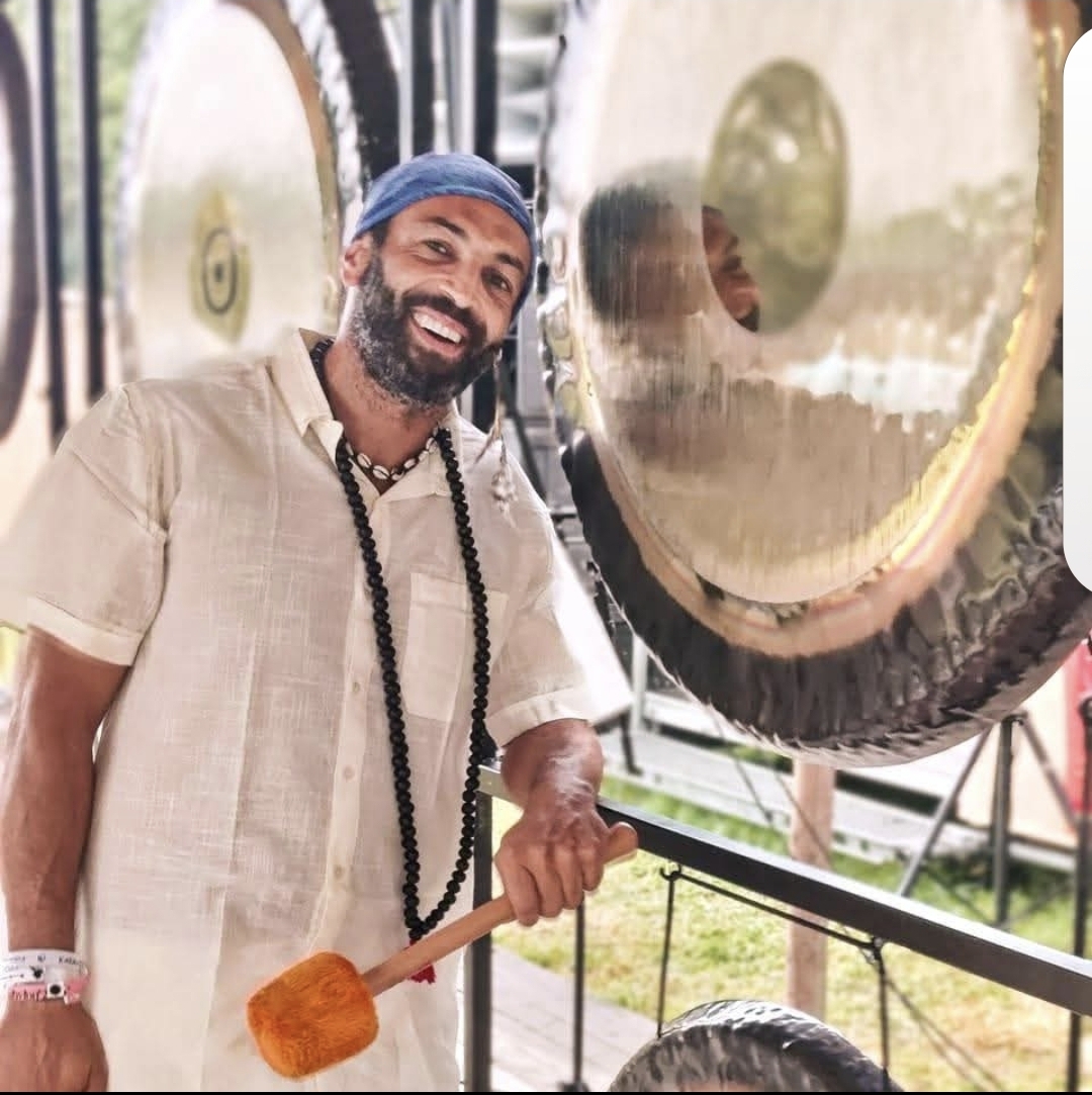 Portrait de Nassim Khabazi souriant devant ses gongs, maillet à la main
